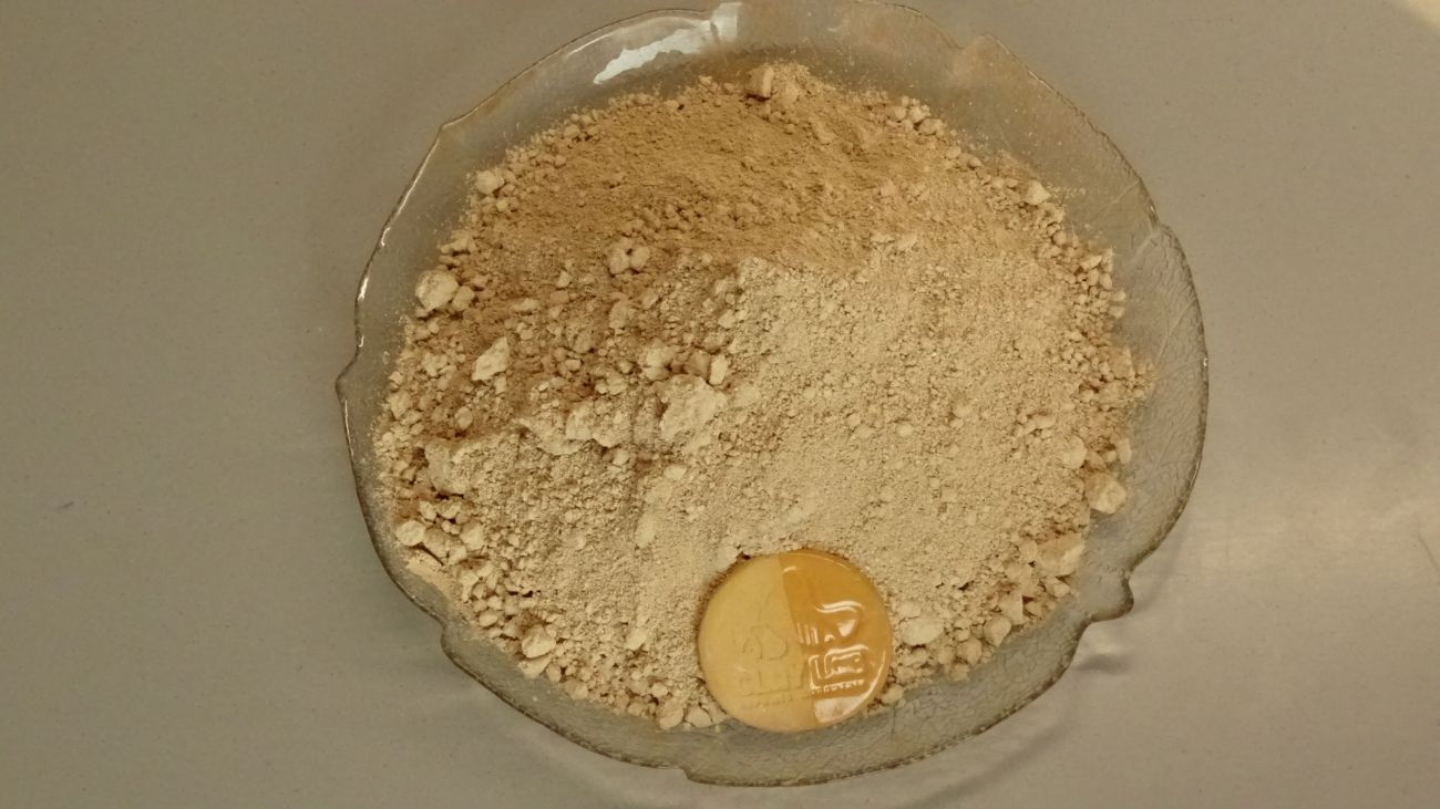 Top view of raw orange clay in a plate with a coin showing its actual color