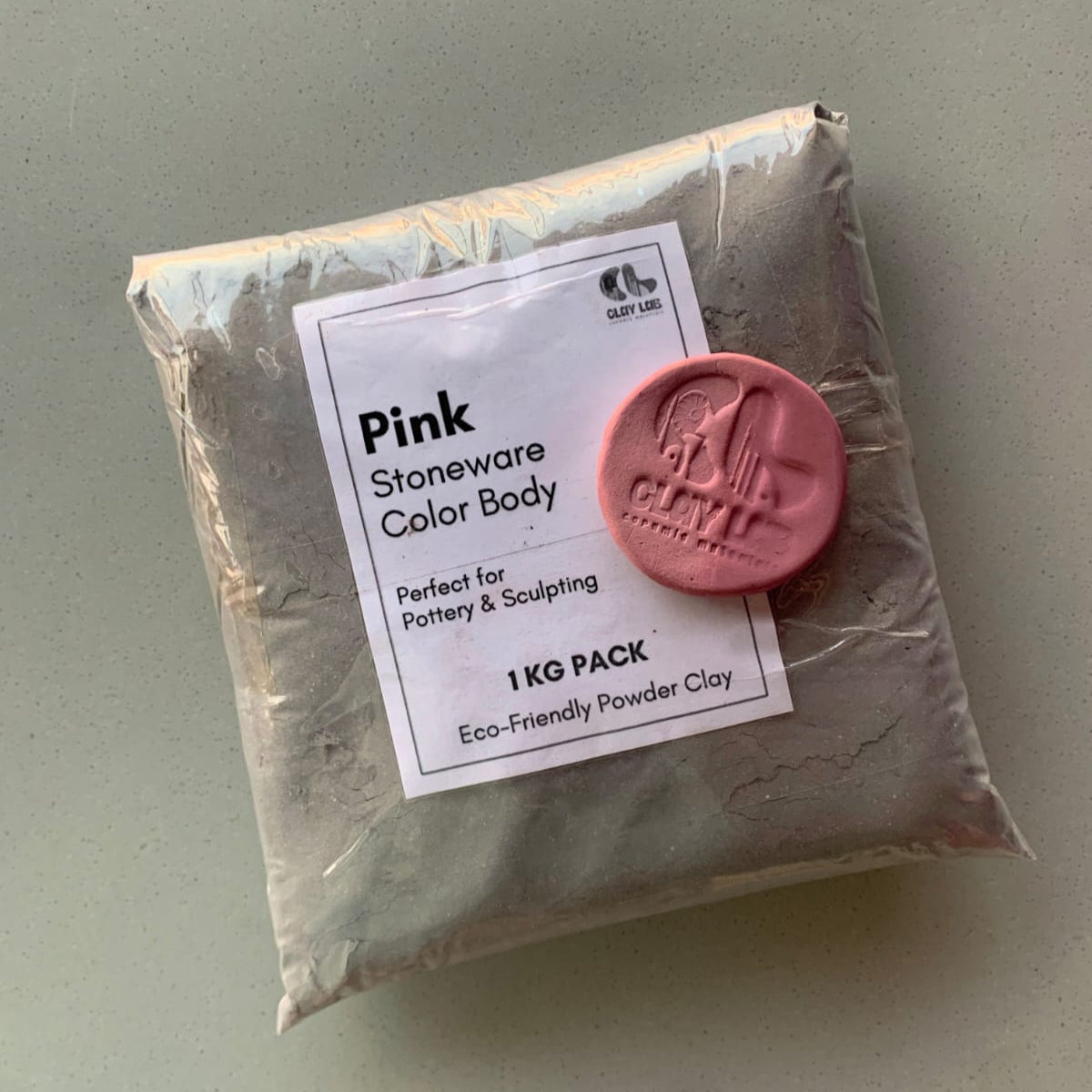 A sealed 1kg bag of pink stoneware color clay, showing its usage and a coin for its actual color 